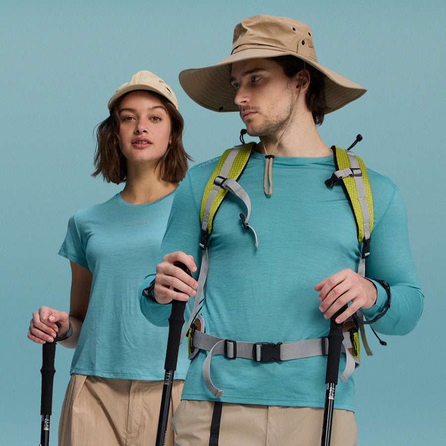 Two people in hiking gear with backpacks and walking sticks against a blue background